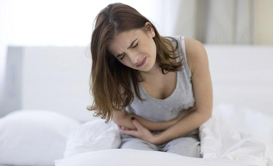 woman on bed gripping stomach