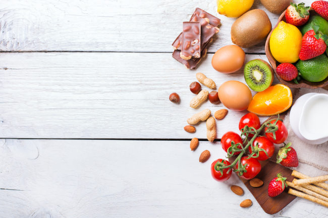 Selection of allergy food, orange citrus juice milk red tomato strawberry kiwi eggs chocolate nuts bread gluten on a rustic wooden table. Copy space background, top view flat lay overhead