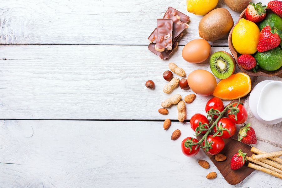 Selection of allergy food, orange citrus juice milk red tomato strawberry kiwi eggs chocolate nuts bread gluten on a rustic wooden table. Copy space background, top view flat lay overhead