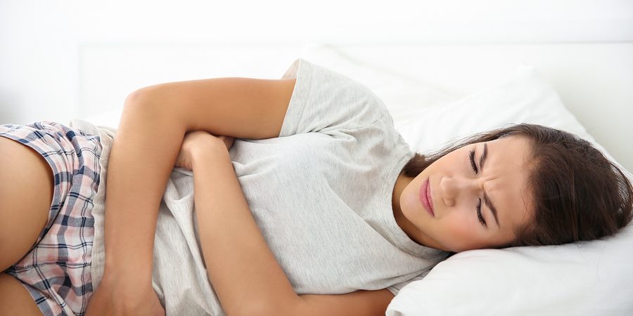 Young woman with stomach ache lying on bed