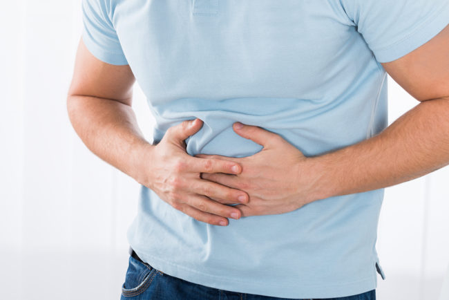 Close-up Of Young Man Suffering From Stomach Ache Standing At Home