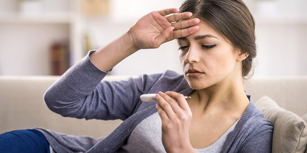 Young woman is looking at the thermometer. She has fever.