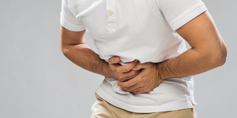 close up of man suffering from stomach ache over gray background