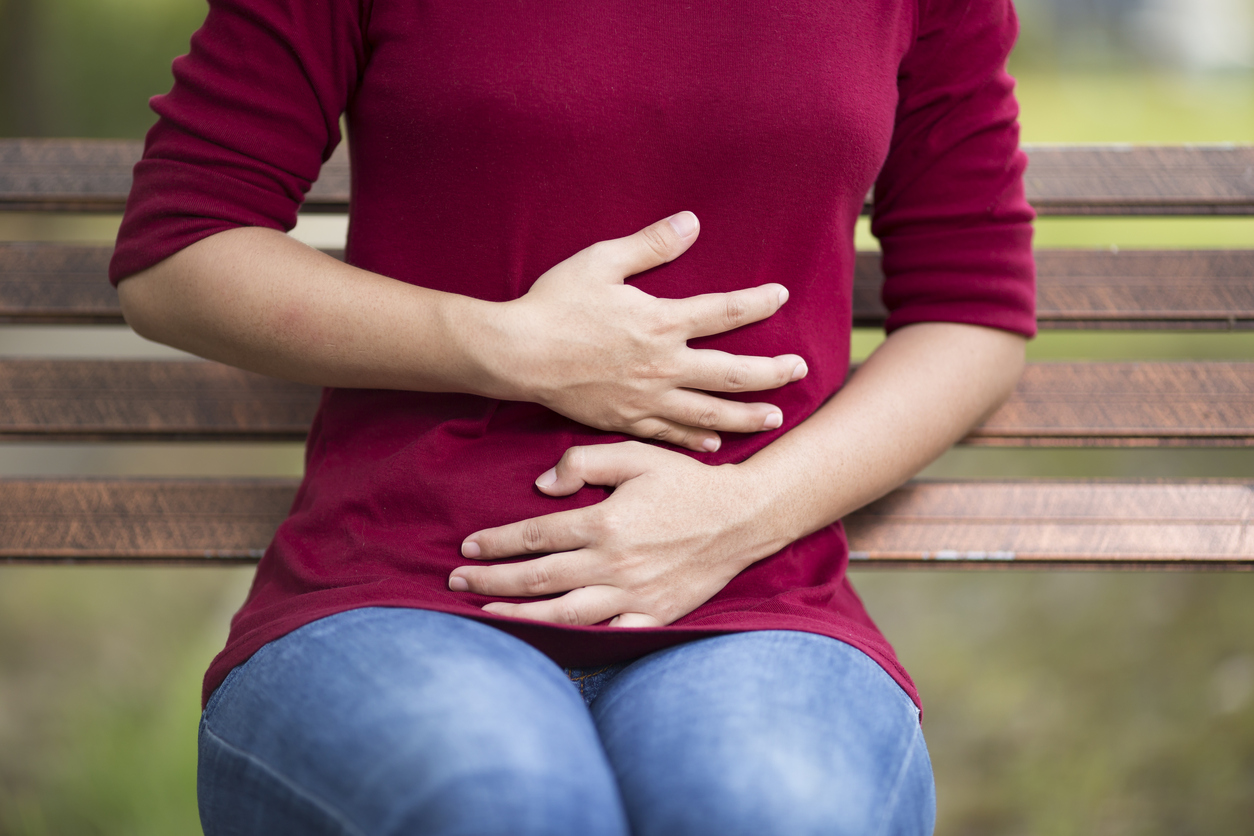 Woman Has Stomach Ache Sitting on Bench at Park