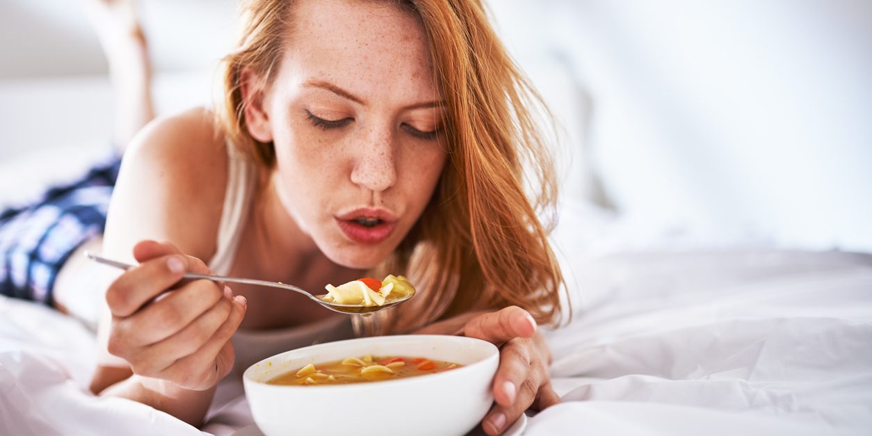 woman blowing on soup to cool it down in bed