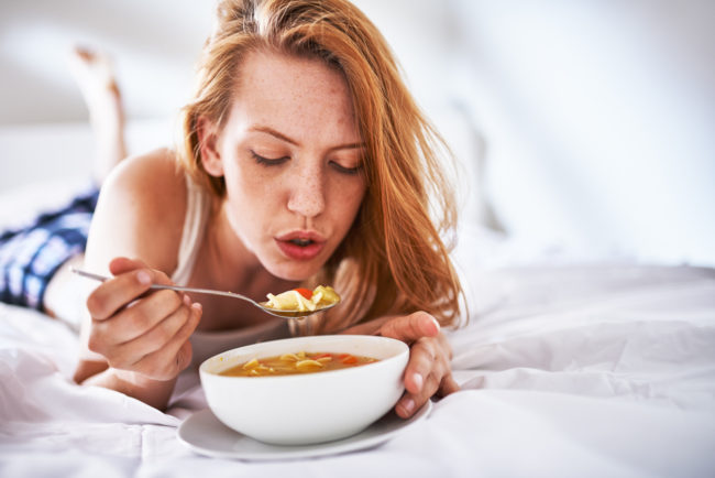 woman blowing on soup to cool it down in bed