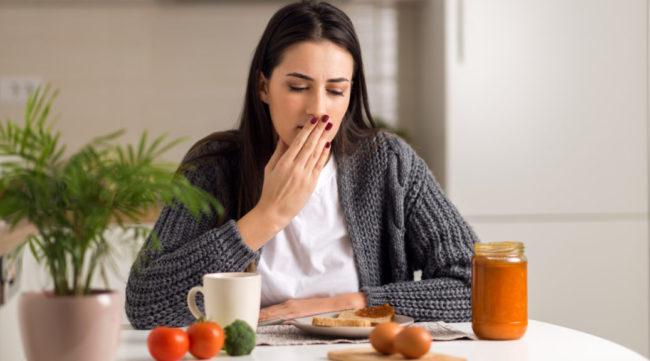young woman covering mouth with hand in front of breakfast