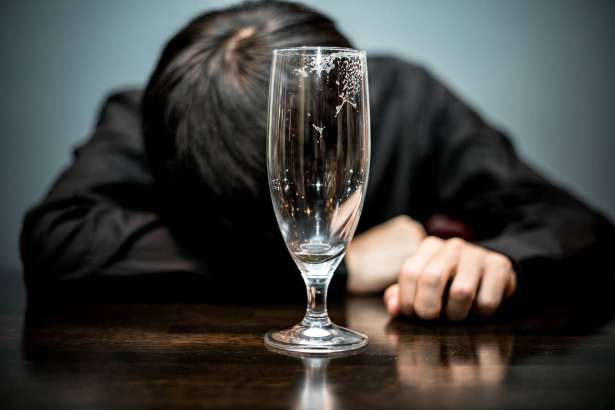 man lying facedown on table, with empty bottle in front of him