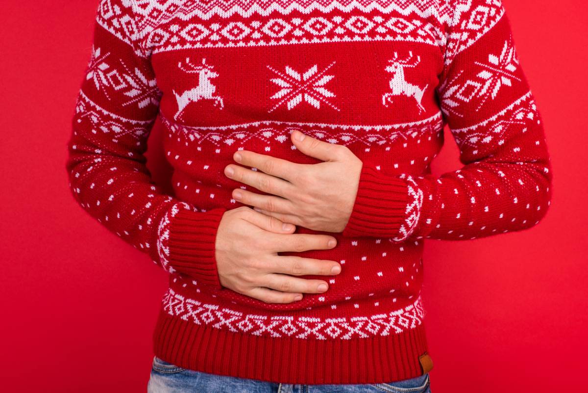 man in christmas sweater against red background gripping abdomen